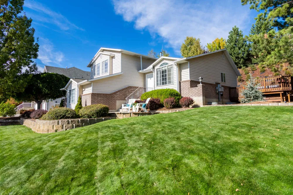 A suburban house on a raised plot with its front lawn falling away in a continuous grass slope down to the street level